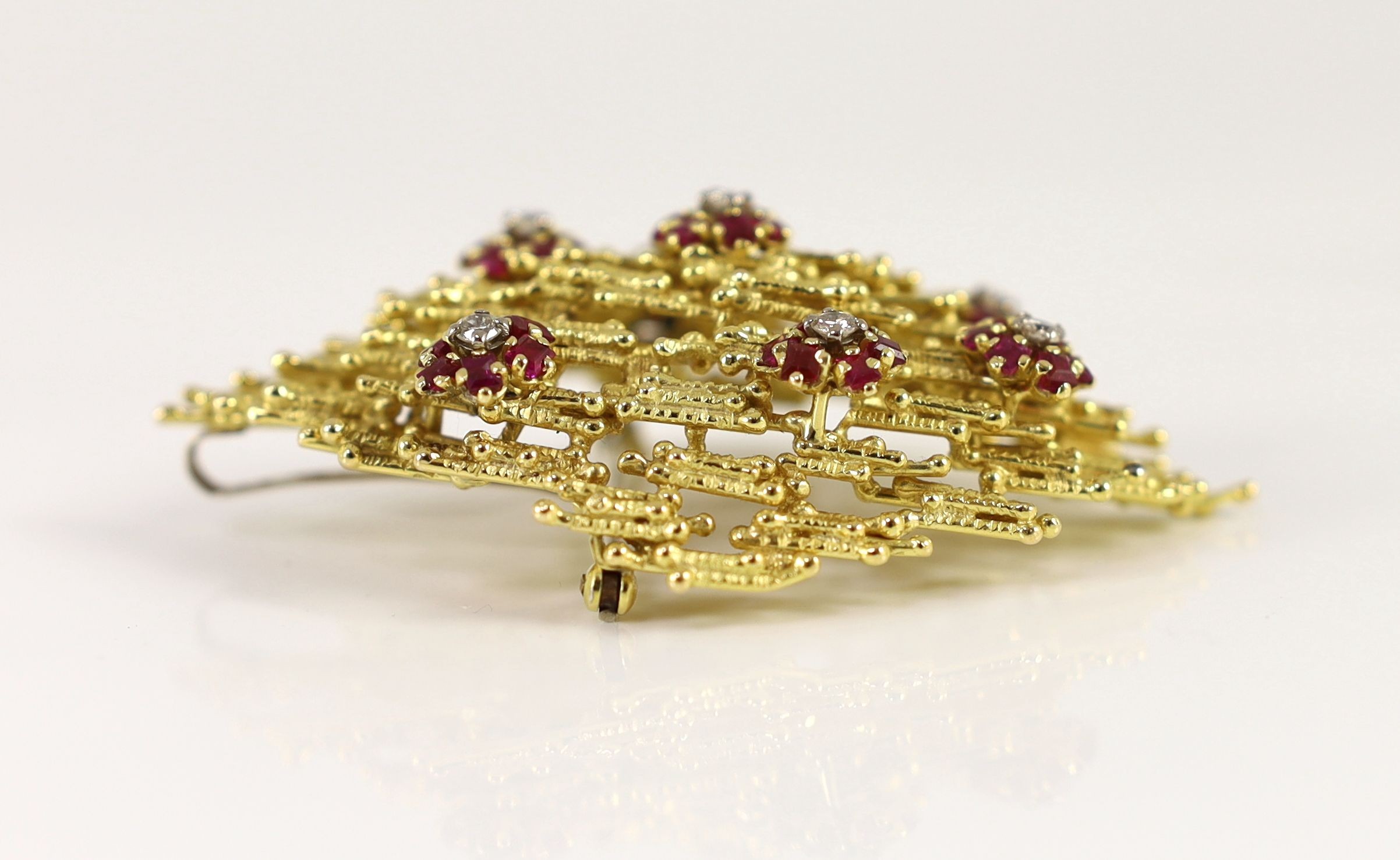 A 1970's textured gold, ruby and diamond cluster set modernist pendant brooch, in the manner of Andrew Grima